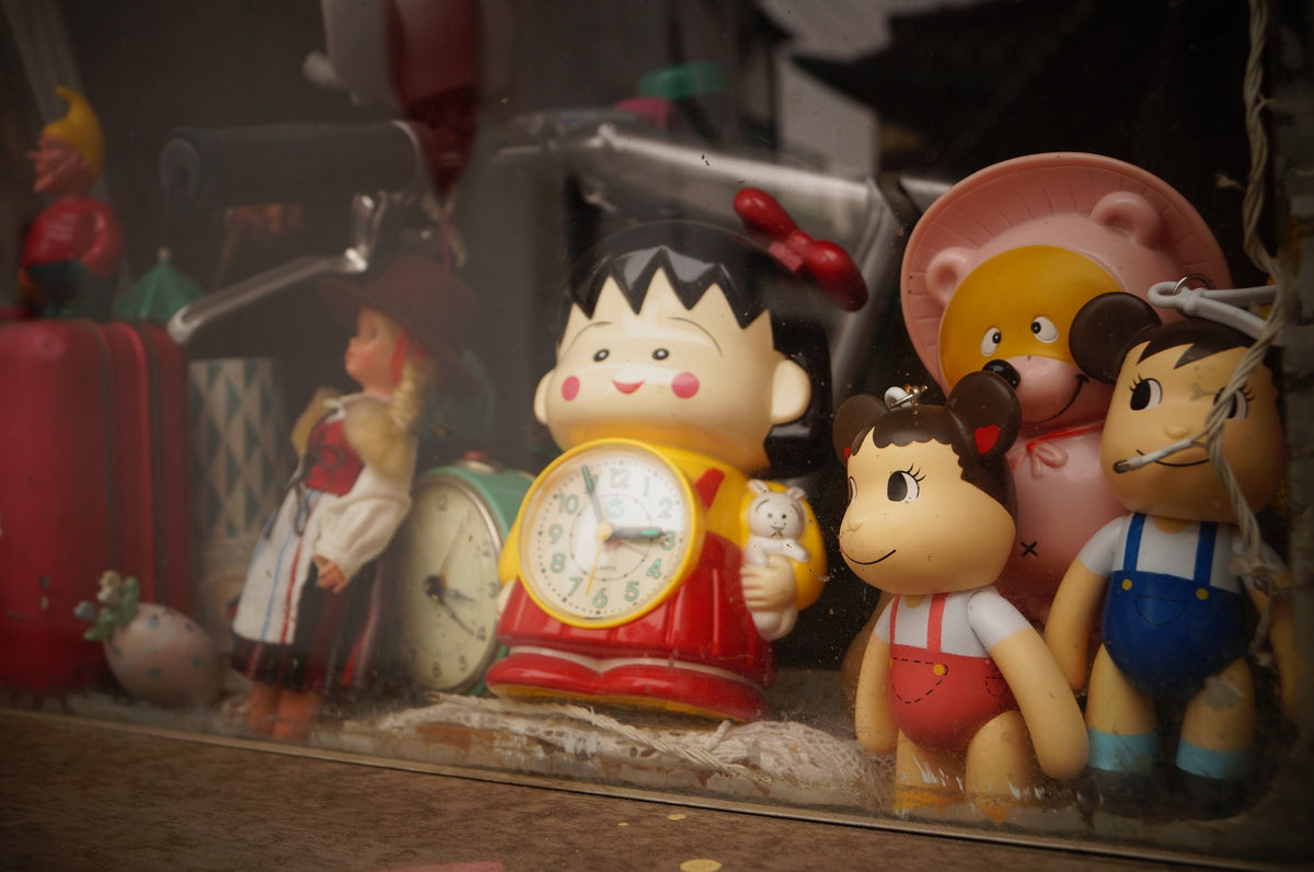 A collection of toys are displayed in a shop window, including a child's toy clock in the center. There are several ways to help your 3-year-old to understand time concepts.
