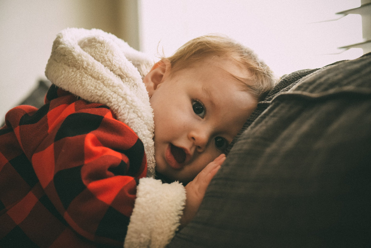 1-year-old in flannel jacket has mouth open as if to say something. You can support your 1-year-old's language development with the use of intentional phrases.