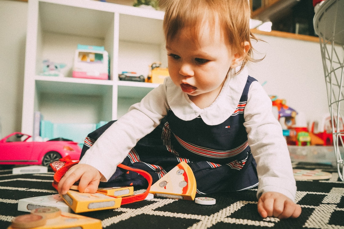 2-Year-Old girl plays on the floor with wooden toys. Toys that aren't too overstimulating are best to gift to young children, as they promote creativity and cognitive development.