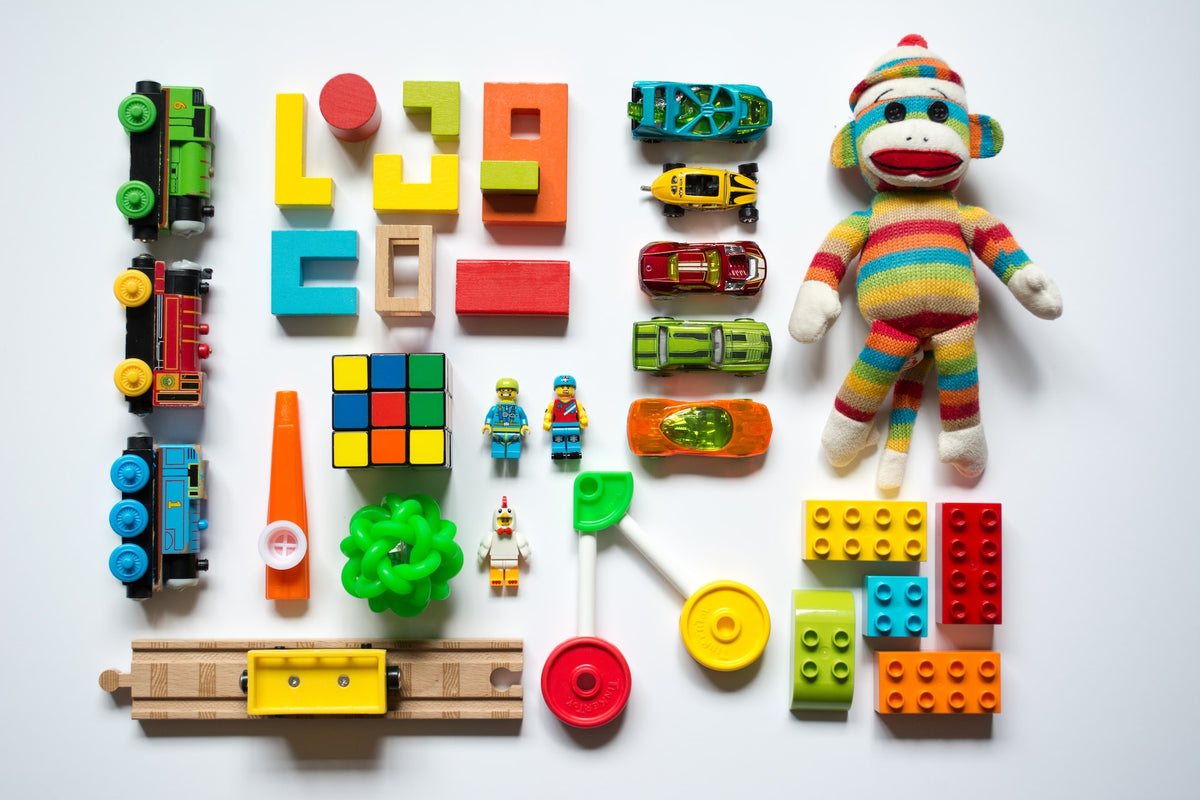An array of colorful toys are arranged carefully on a white background. Keeping toys organized through toy rotation is an easy way to combat overwhelm and avoid overstimulating your child.