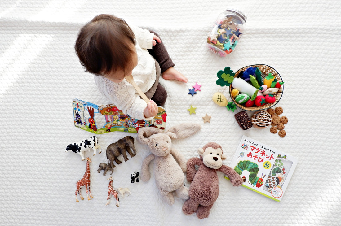 1-year-old child sits with toys and board books scattered about him. Children as young as 1 can begin developing print awareness by being exposed to books during playtime.